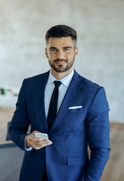 Man in a blue suit holding a smartphone indoors